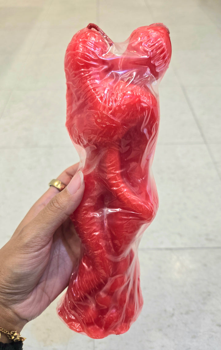 Hand holding a large red candle in the shape of an intertwined couple sharing an embrace